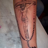 Religious gray-ink Jesus on cross with beads tattoo on forearm