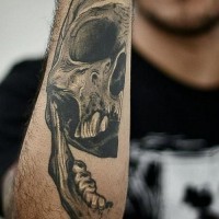 Tattoo von  angsteinflößender Totenkopfhälfte in grauer Tusche  am Unterarm