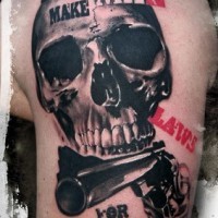 Sharp designed big realistic skull with lettering and pistol tattoo on shoulder
