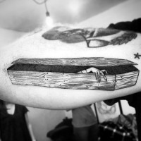 Simple black and white wooden coffin with zombie hand tattoo on arm