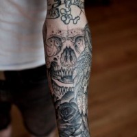 Simple black ink little skull with lettering tattoo on arm