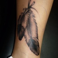 Tatuaje en la pierna, dos plumas negras grises