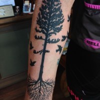 Simple painted black ink tree with roots tattoo on forearm combined with flying birds