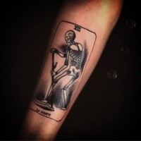Small black ink arm tattoo of card stylized with skeleton and lettering