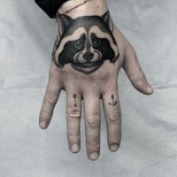 Small black ink cute looking hand tattoo of raccoon with symbols