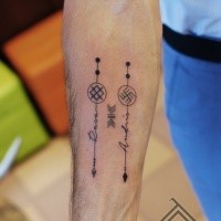 Small black ink forearm tattoo of arrows with lettering and symbols