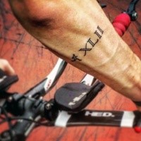 Small black ink numbers with running man tattoo on forearm