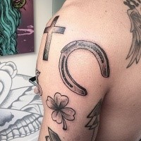 Small black ink shoulder tattoo of cross with horseshoe and clover
