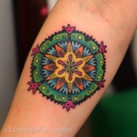 Small cartoon style colored ornamental flower tattoo on forearm