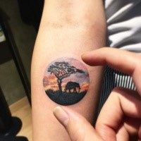 Small circle shaped colored forearm tattoo of elephant with lonely tree