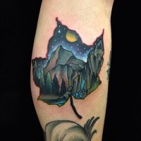 Small colored maple leaf shaped tattoo on leg stylized with night mountains