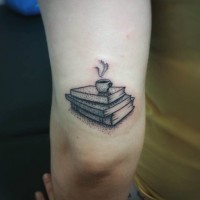 Tatuaje en el brazo,
pila de libros sencillos con taza de té