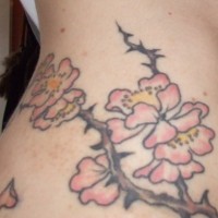 Tattoo von dornigem Zweig mit rosa Blumen an der Hüfte