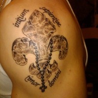 Tatuaje en el brazo,
 flor de lis de piedra con cruz y inscripción