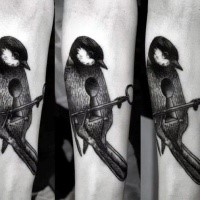 Impresionante tatuaje de antebrazo de tinta negra de pájaro combinado con llave y ojo de cerradura
