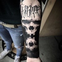 Stunning blackwork style forearm tattoo of mirrored skulls with lettering