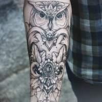 Stylized black owl tattoo on forearm