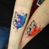 Tatuagem de antebraço com aspecto simétrico e colorido de cabeças de gato com estrelas