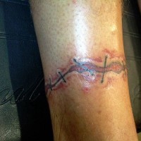 Tattoo von grob genähter Wunde in der Knöchelgegend