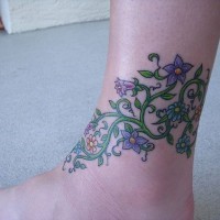 Tattoo von Pflanze mit lila Blümchen in der Knöchelgegend