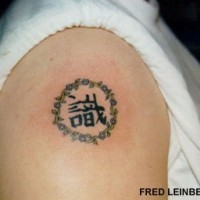 Tatuaje en el hombro de jeroglíficos asiáticos en circulo.