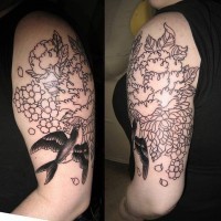 Tatuaje en el brazo, ave negro con flores descoloridos