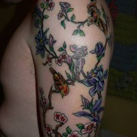 Tatuaje en el brazo, rama con montón de flores y aves en elle dibujo multicolor