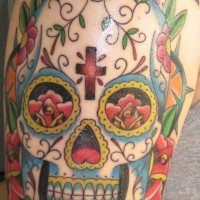 el tatuaje de una calavera mexicana con una cruz en sy frente hecho en el hombro con tinta de varios colores