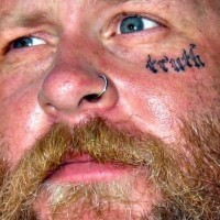 Tatuaje en la cara, inscripción diminuta, verdad
