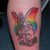 Tatuaje de una hada con alas color arco iris sentada sobre setas