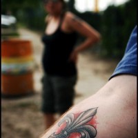 Tatuaje flor de lis con sombra roja en mano