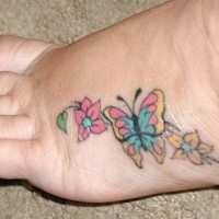 Un papillon avec des fleurs le tatouage sur le pied en couleurs