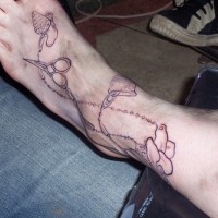 Chaînes avec des ciseaux et doigtier le tatouage sur le pied