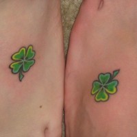 Tattoo von zwei kleinen grünen saftigen Kleeblättern mit vier Blütenblättern auf Füßen