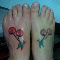 Dos cerezas con hojas verdes tatuados en cada pie