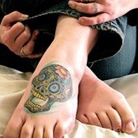 Tattoo von grünem Totenkopf mit gelben Zehnen auf dem Fuß