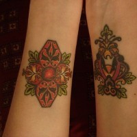 Tattoo von zwei malerischen Zeichen mit Blättern und Schnörkeln am Unterarm