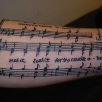 Sheet music, text of song forearm tattoo