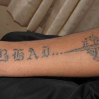 La daga e la scritta in lingua straniere tatuati sul braccio