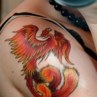 el tatuaje hermoso de la ave fenix de color naranja hecho en el hombro