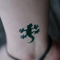El tatuaje pequeño de una lagartija negra en la pierna
