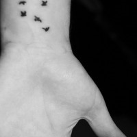 Tatuaje en la mano, varias aves negas muy pequeñas