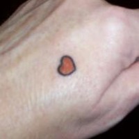 Tatuaje en la mano, corazón rojo con contornos negros, diseño muy diminuto