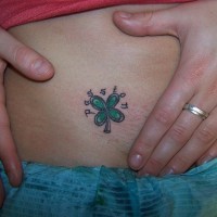 Tattoo von kleinem grünem schönem Kleeblatt mit einem Namen an der Hüfte