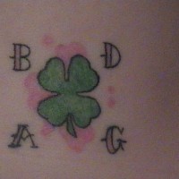 Tattoo von grünem stilisiertem Kleeblatt und Buchstaben an der Hüfte