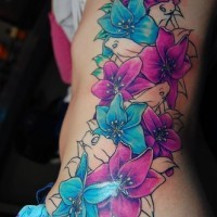 Großes Tattoo von malerischen blauen und lila Blumen an der Hüfte