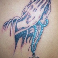 el tatuaje de las manos orantes con un rosario azul