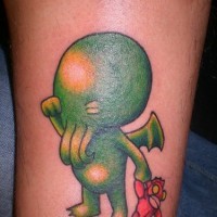 Un monstre bébé vert tatouage sur le mollet criant avec une jouette