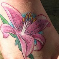 El tatuaje de un Lirio rosa con estambres de color blanco y amarillo y unas hojas alrededor
