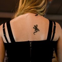 El tatuaje pequeño de una lagartija de color negro en la espalda